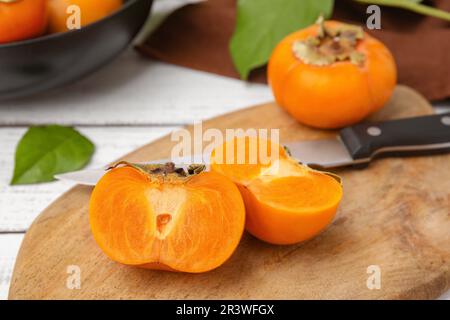 Ganze und geschnittene köstliche reife Persimonen auf einem weißen Holztisch Stockfoto