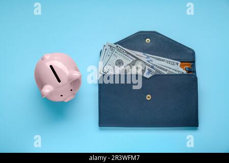 Sparschwein und Geldbörse mit Banknoten auf hellblauem Hintergrund, flach liegend Stockfoto