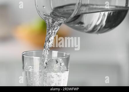 Wasser aus der Kanne auf unscharfem Hintergrund in Glas gießen, schließen Stockfoto