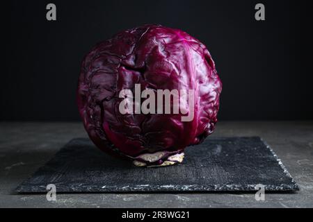 Ein frischer, reifer Rotkohl mit Wassertropfen auf einem grauen Tisch vor dunklem Hintergrund Stockfoto