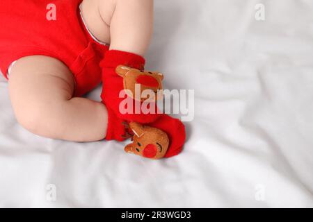 Baby trägt festliche Weihnachtssocken auf weißem Bettlaken, Nahaufnahme. Platz für Text Stockfoto