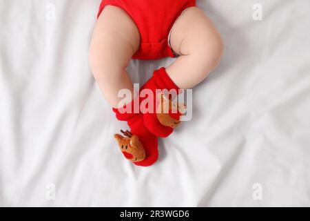 Baby trägt festliche Weihnachtssocken auf weißem Bettlaken, Draufsicht Stockfoto