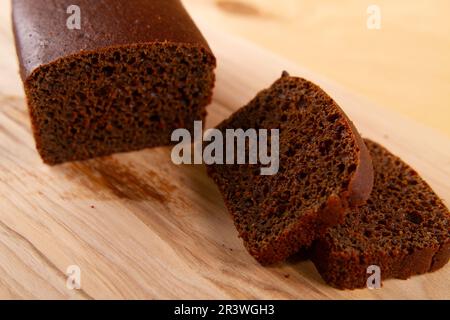 Dunkles Brot in Laib- und Schnittform auf hellbeige Holzfläche. Selektiver Fokus Stockfoto