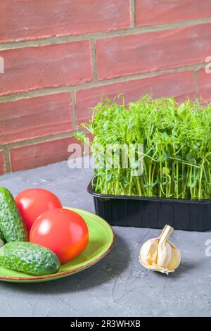 Erbsen in der Küche. Frischer Salat, Gurken, Tomaten. Das Konzept der gesunden Ernährung. Backsteinwände. Stockfoto