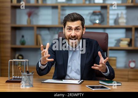 Verärgerter und schreiender Geschäftsmann im Büro, der sich per Videoanruf unterhält, der Chef schrie in einem Online-Meeting mit Kollegen und Untergebenen, unzufrieden mit der Arbeit von Kollegen und Partnern. Stockfoto