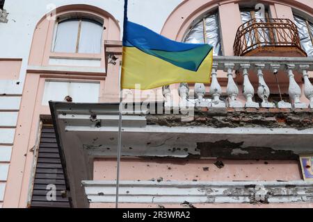 OKHTYRKA, UKRAINE - 24. MAI 2023 - Eine ukrainische Flagge fliegt außerhalb eines Gebäudes im Stadtzentrum, das durch russischen Granatwerfer beschädigt wurde, Okhtyrka, Sumy Region, No Stockfoto