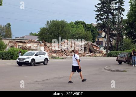OKHTYRKA, UKRAINE - 24. MAI 2023 - Ein Mann überquert eine Straße in der Nähe eines Gebäudes, das von russischen Granaten zerstört wurde, Okhtyrka, Sumy Region, Nordostukraine. Stockfoto