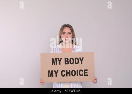 Frau hält Plakat mit Phrase Mein Körper Meine Wahl auf hellgrauem Hintergrund. Schwangerschaftsabbruch-Protest Stockfoto