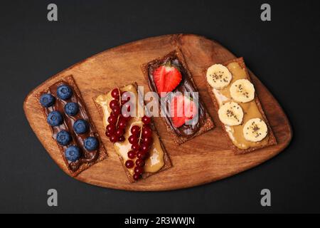 Frisches knuspriges Roggen-Knusperbrot mit verschiedenen Belägen auf schwarzem Tisch, Draufsicht Stockfoto