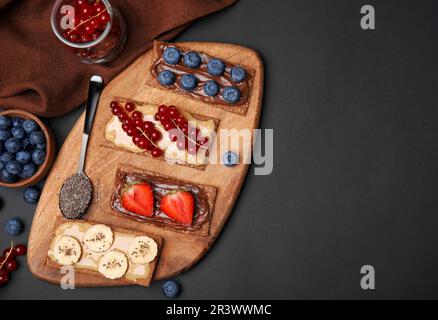 Frisches knuspriges Roggen-Knusperbrot mit verschiedenen Belägen auf einem schwarzen Tisch, flach liegend. Platz für Text Stockfoto