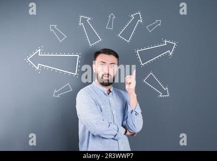Berufswahl oder andere Lebensbereiche, Konzept. Entscheidungen treffen, emotionaler Mann, umgeben von gezeichneten Pfeilen auf grauem Hintergrund Stockfoto
