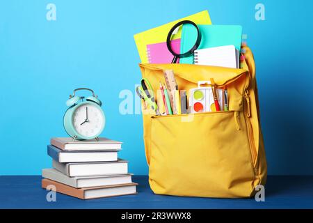 Gelber Rucksack und verschiedene Schreibwaren auf blauem Holztisch Stockfoto