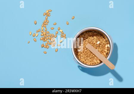 Holzstäbchen zum Auftragen von Wachs und gelbem Wachsgranulat für kosmetische Verfahren auf blauem Hintergrund, Draufsicht Stockfoto