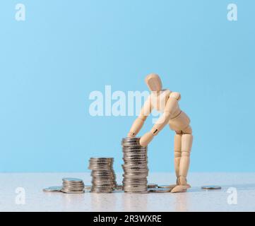 Eine Schaufensterpuppe aus Holz und ein Münzstapel auf blauem Hintergrund Stockfoto