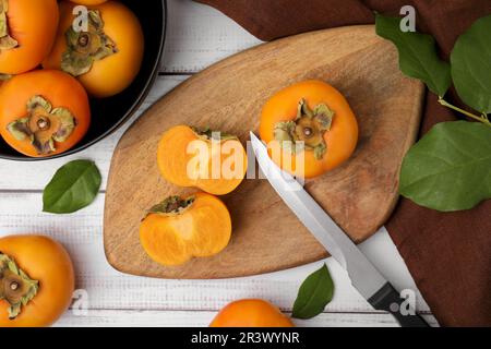 Ganze und geschnittene köstliche reife Persimonen auf weißem Holztisch, flach liegend Stockfoto