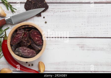 Scheiben von köstlichem Rinderjerky und Zutaten auf weißem Holztisch, flach liegend. Platz für Text Stockfoto