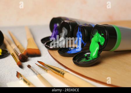 Tuben mit bunten Farben und Pinseln auf einem strukturierten Tisch, Nahaufnahme Stockfoto