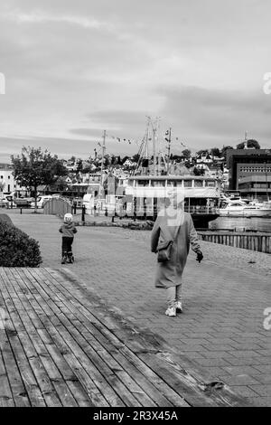 Sandnes, Norwegen, Mai 18 2023, Mutter und Kind, die alleine entlang der Sandnes Harbour Waterfront mit Vergnügungsbooten im Hintergrund spazieren Stockfoto