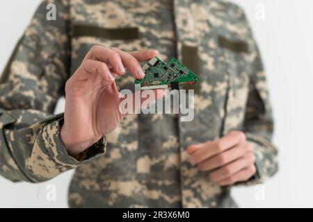 Ein Soldat hält einen Chip in der Hand. Mikroschaltungen, grüne Tarnung. Stockfoto