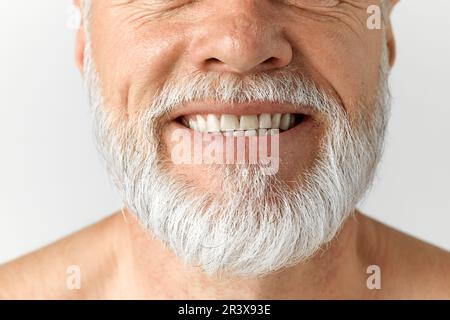 Nahaufnahme des grauen Männerbarts. Reifes männliches Modell, das vor grauem Hintergrund lächelt. Zahnpflege Stockfoto
