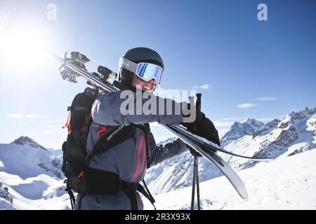 Französische Alpen, Serre-Chevalier: Frau, Skifahrerin mit Helm und Sonnenbrille mit ihren Skiern auf der Schulter. Übung von Skitouren (Langlauf Stockfoto
