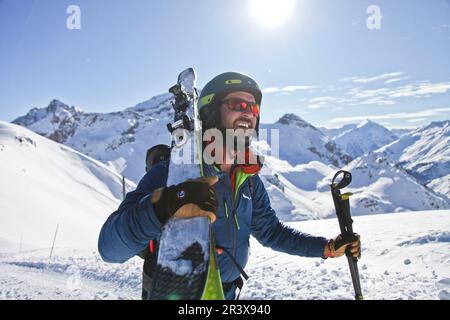 Französische Alpen, Serre-Chevalier: Skifahrer mit Helm und Sonnenbrille, der mit seinen Skiern auf der Schulter spaziert. Übung von Skitouren (Skilanglauf) Stockfoto