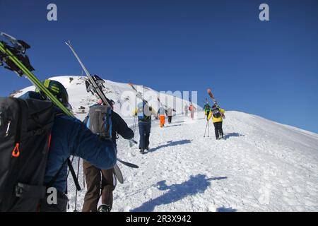 Französische Alpen, Serre-Chevalier: Eine Gruppe von Skifahrern mit Helmen und Sonnenbrillen, die mit ihren Skiern auf den Schultern laufen. Übung von Skitouren (Cross-c Stockfoto