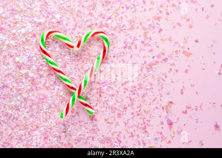 Herz aus zwei Lutschern auf rosa Hintergrund mit Glitzer. Geschenke für das neue Jahr und Weihnachten. Flat Lay Stockfoto