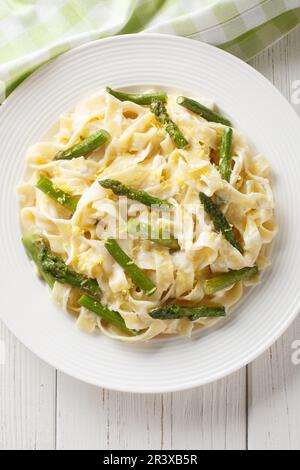 Zitronenspargel Pasta fettuccine mit Parmesan-Sahne-Sauce auf dem Teller auf dem Holztisch. Vertikale Draufsicht von oben Stockfoto