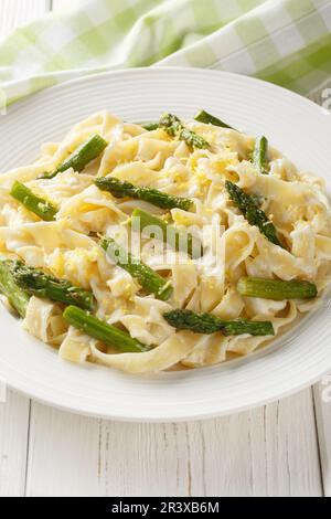 Fettuccine Pasta mit Spargel, Zitrone in einer cremigen Käsesauce, Nahaufnahme auf einem Teller auf dem Tisch. Vertikal Stockfoto
