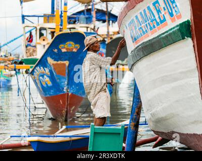 Ein Mann, der an einem Fischereifahrzeug in einer einfachen Werft am Strand in Tinoto, Maasim, in der Provinz Sarangani auf den Philippinen lackiert. Stockfoto