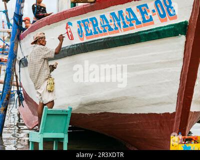 Ein Mann, der an einem Fischereifahrzeug in einer einfachen Werft am Strand in Tinoto, Maasim, in der Provinz Sarangani auf den Philippinen lackiert. Stockfoto