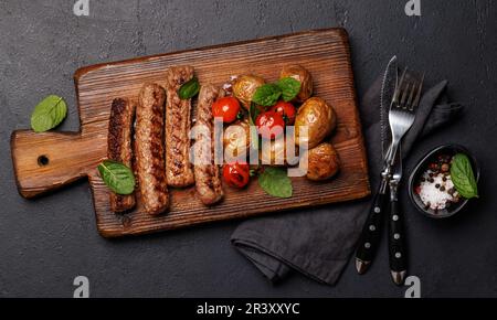 Köstliche gegrillte Würstchen und Kartoffeln auf einem Holzbrett. Flach verlegt Stockfoto