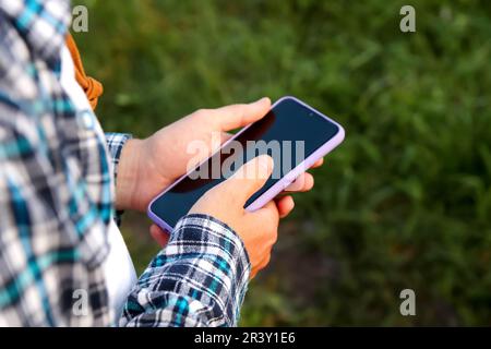 Die männliche Hand des Bauern benutzt das Telefon. Im Außenbereich werden bei einer Nahaufnahme die Hände eines männlichen Kaukasiers erfasst, der fest an einem Smartphone greift Stockfoto
