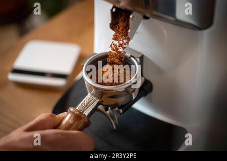 Großaufnahme gemahlener Arabica-Kaffee aus einer elektrischen Mahlmaschine im Portafilter bereit für die Zubereitung guter Espresso-Mahlmaschine Kaffeeextraktion Stockfoto