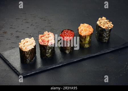 Set aus Gunkan Maki Sushi mit verschiedenen Arten von Fisch (Lachs, Jakobsmuscheln, Barsch, Aal, Garnelen) und Kaviar auf schwarzem Hintergrund. Trad Stockfoto