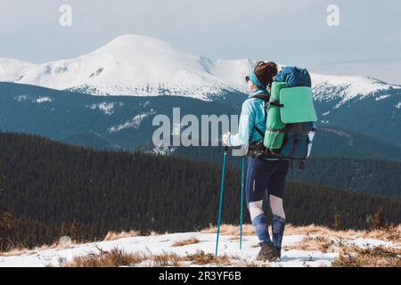 Ein Wanderer mit einem großen Rucksack steht und bewundert die verschneiten Berge. Wandern in den Karpaten. Stockfoto