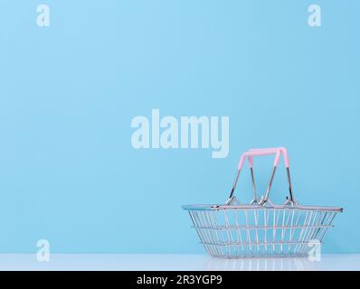 Leerer Miniatur-Einkaufswagen aus Metall für den Supermarkt auf blauem Hintergrund Stockfoto