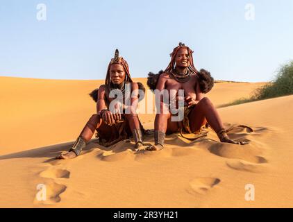 Zwei Himba-Frauen sitzen auf dem Sand in der Wüste. Stockfoto