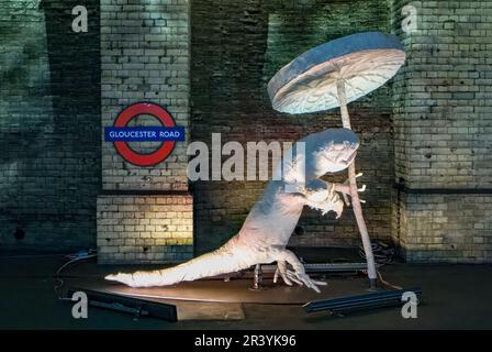 Ein großes Modell eines weißen Salamanders, der eine Riesenlilie auf einem stillgelegten Bahnsteig in der U-Bahn-Station Gloucester Road in London hält. Dieses Fiorm bildet einen Teil der Stockfoto