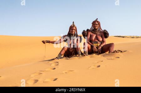 Zwei Himba-Frauen sitzen auf dem Sand in der Wüste. Stockfoto