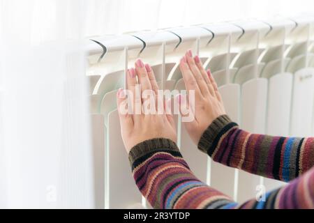 Das Mädchen wärmt die gefrorenen Hände über der heißen Heizung auf, Nahaufnahme Stockfoto