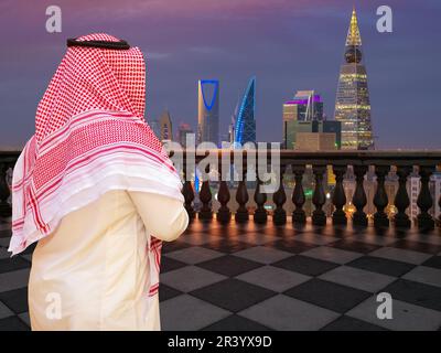 Ein Saudi-Mann mit traditionellen Tüchern, der von einer Terrasse (Balkon) eines hohen Gebäudes aus auf Riad City, Saudi-Arabien blickt. Stockfoto