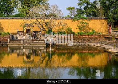 Eine gelbe Mauer, Bäume und ein Schrein, der sich auf einem Teich in der Kaiserstadt spiegelt, Zitadelle von Hue, die antike Hauptstadt von Vietnam. Stockfoto