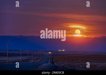 Der Vollmond erhebt sich über einer Landstraße in Alberta, Canda. Stockfoto