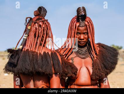 Zwei Frauen des Himba-Stammes sehen sich in traditionellen Kleidern und traditionellen Frisuren gegenüber. Stockfoto
