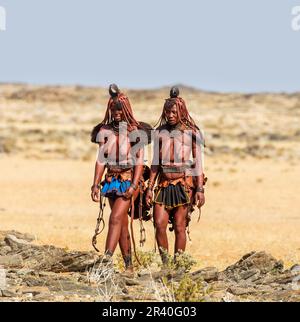 Zwei Frauen des Himba-Stammes laufen in Nationalkleidung durch die Wüste. Stockfoto