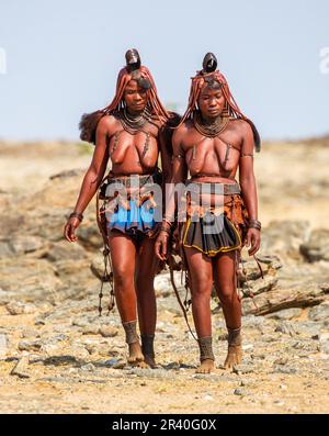 Zwei Frauen des Himba-Stammes laufen in Nationalkleidung durch die Wüste. Stockfoto