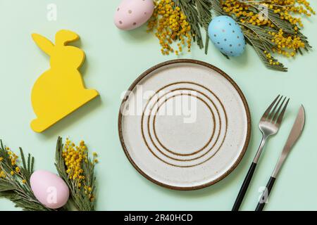 Ostertisch. Teller mit ostereiern und Mimosa auf pastellgrünem Hintergrund. Frohes Osterferienkonzept für das Restaurant Stockfoto