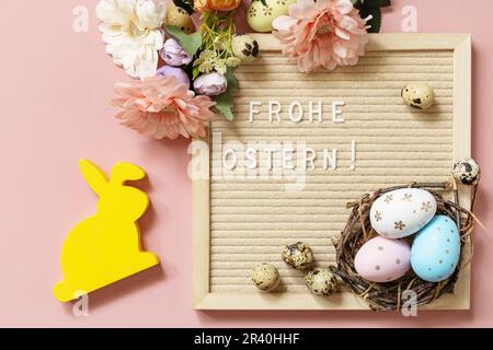 Anschreiben, Frohe Ostern - Happy Easter in deutscher Begrüßung, Ostereier und Frühlingsblumen auf pastellrosa Hintergrund. Ansicht f Stockfoto